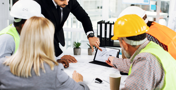 Team of electricians wearing safety gear sitting at a table discussing project details